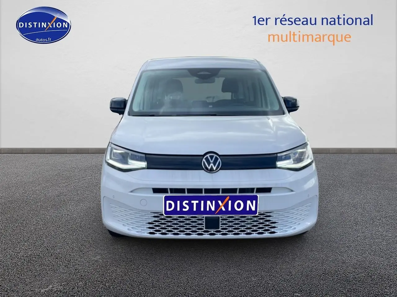 Vue de face du Volkswagen Caddy blanc 2025 avec calandre noire et logo VW centré, sur fond neutre.