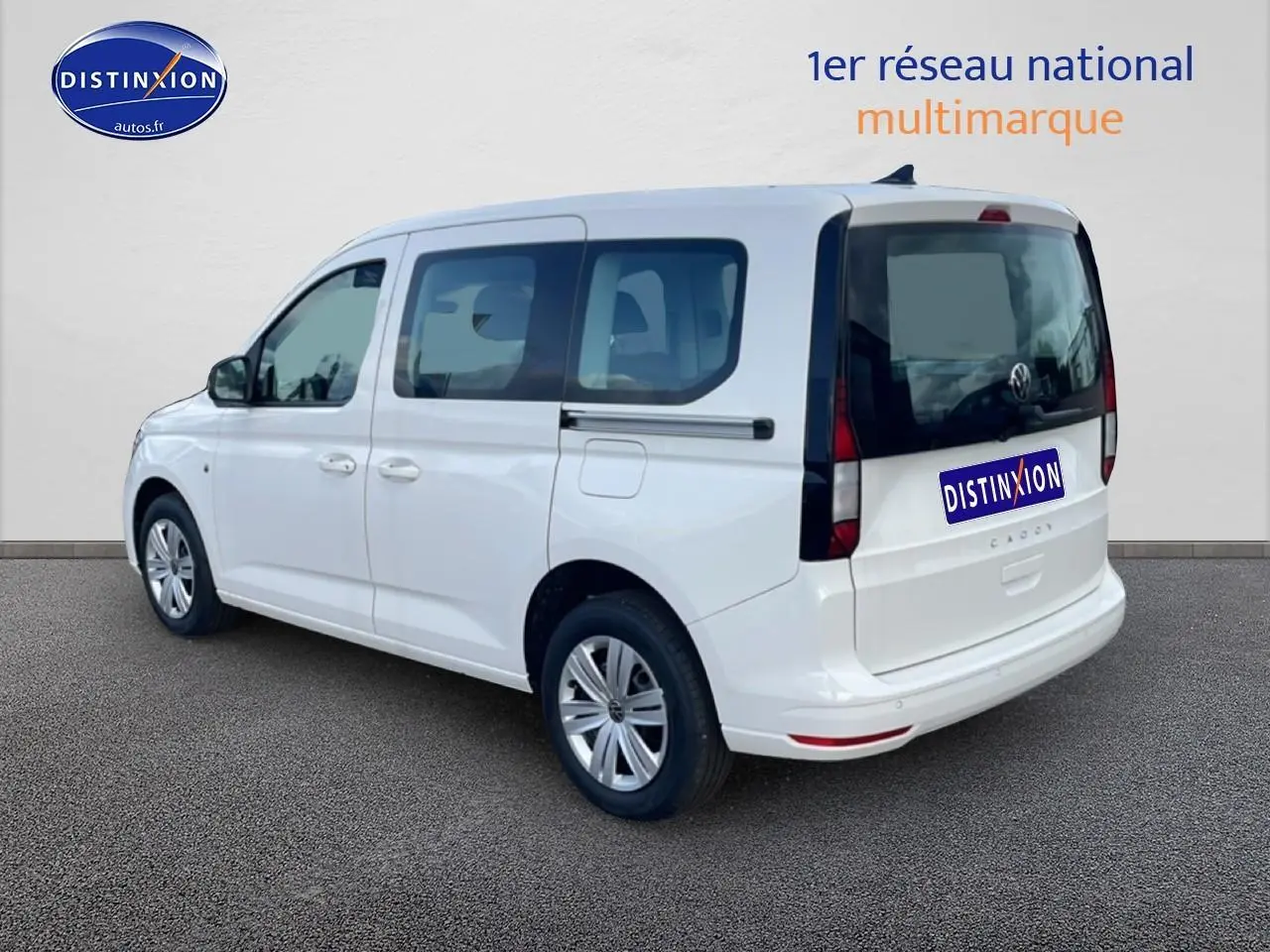 Vue 3/4 arrière droite d'un Volkswagen Caddy blanc 2025 avec vitres teintées et barres de toit visibles.