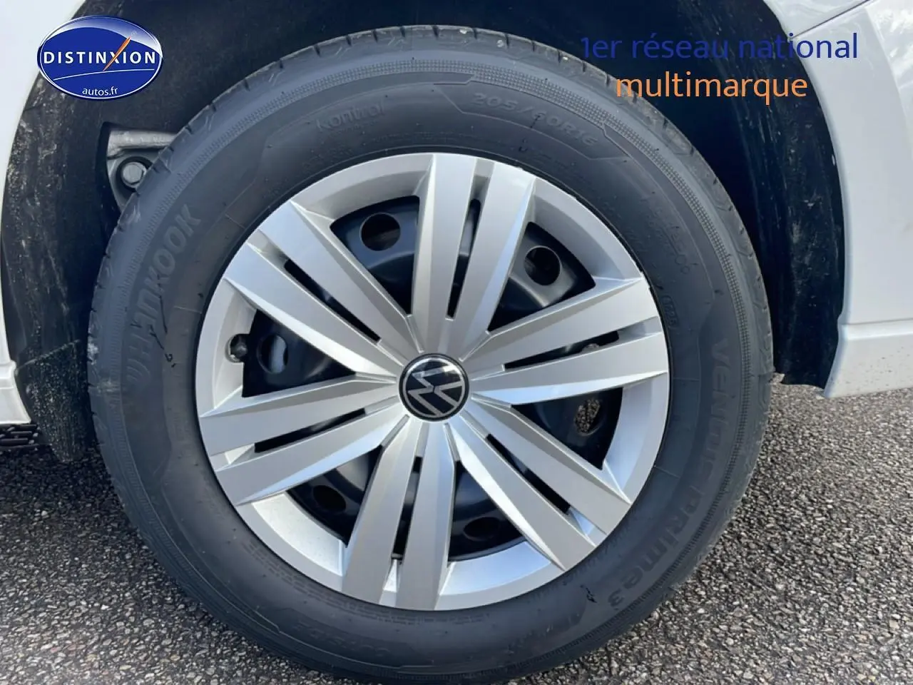 Gros plan sur la roue avant droite d’un Volkswagen Caddy blanc avec jante argentée et logo VW central.