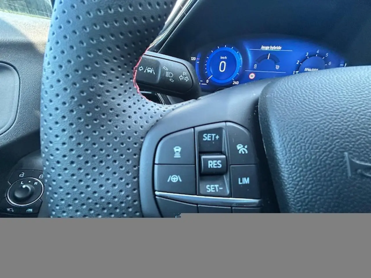 Gros plan sur le volant perforé avec surpiqûres rouges et le combiné numérique bleu du Ford Puma II gris Magnetic, version ST-Line.