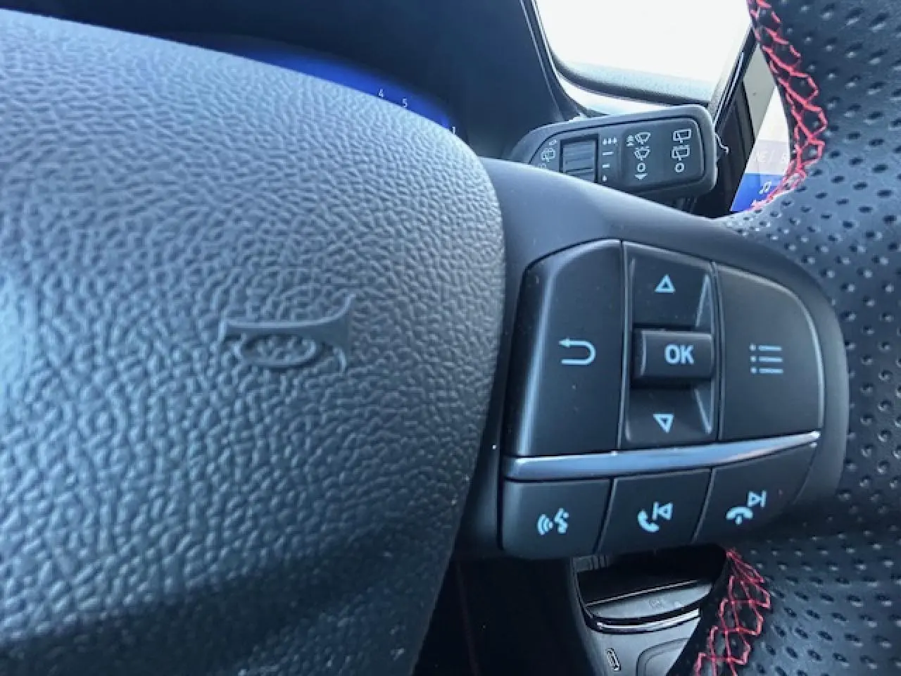 Gros plan sur le volant perforé avec surpiqûres rouges du Ford Puma gris Magnetic, montrant les commandes multifonctions.