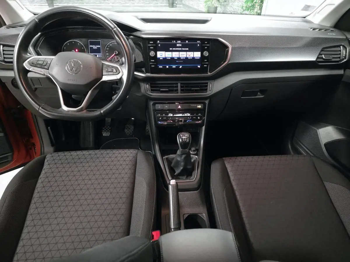 Vue intérieure frontale du tableau de bord et volant cuir noir du Volkswagen T-Cross 1.0 TSI 110 Active, avec levier de vitesses manuel.