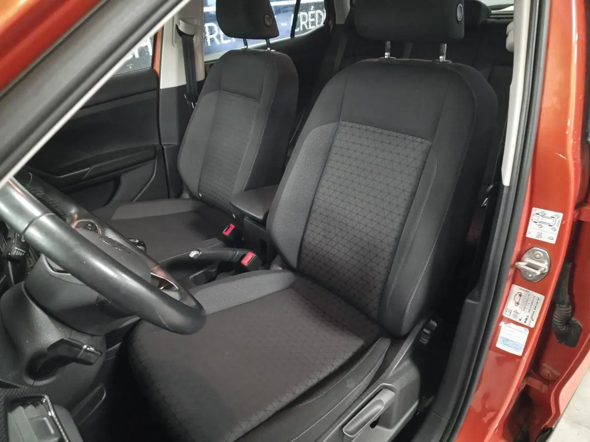Vue intérieure côté conducteur du Volkswagen T-Cross orange, mettant en valeur les sièges avant en tissu noir avec motifs géométriques.