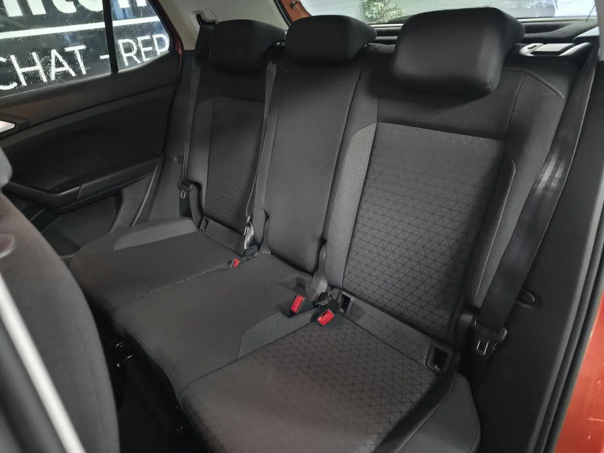 Vue intérieure montrant la banquette arrière noire du Volkswagen T-Cross orange, avec appuis-tête et ceintures visibles.