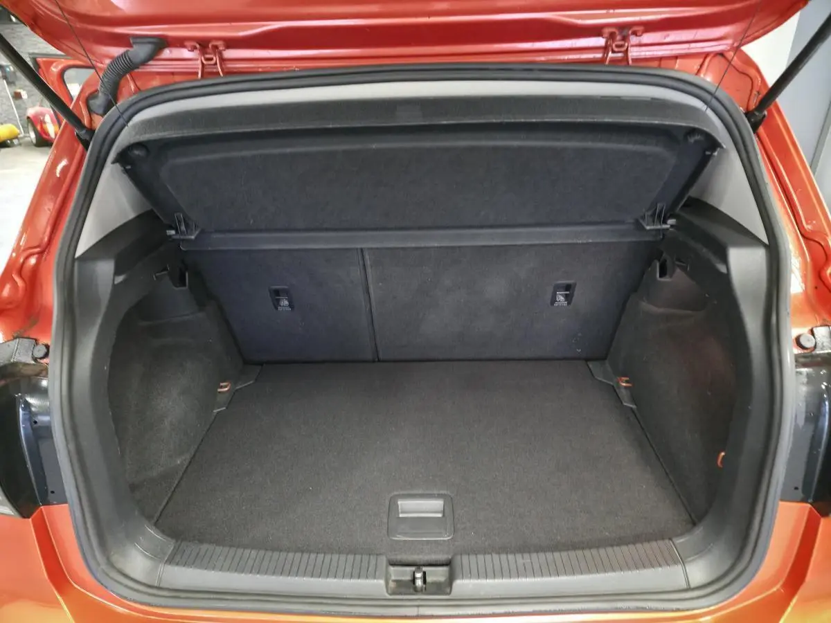 Coffre ouvert d'un Volkswagen T-Cross orange, vue arrière montrant l'espace de chargement vide et la tablette cache-bagages.