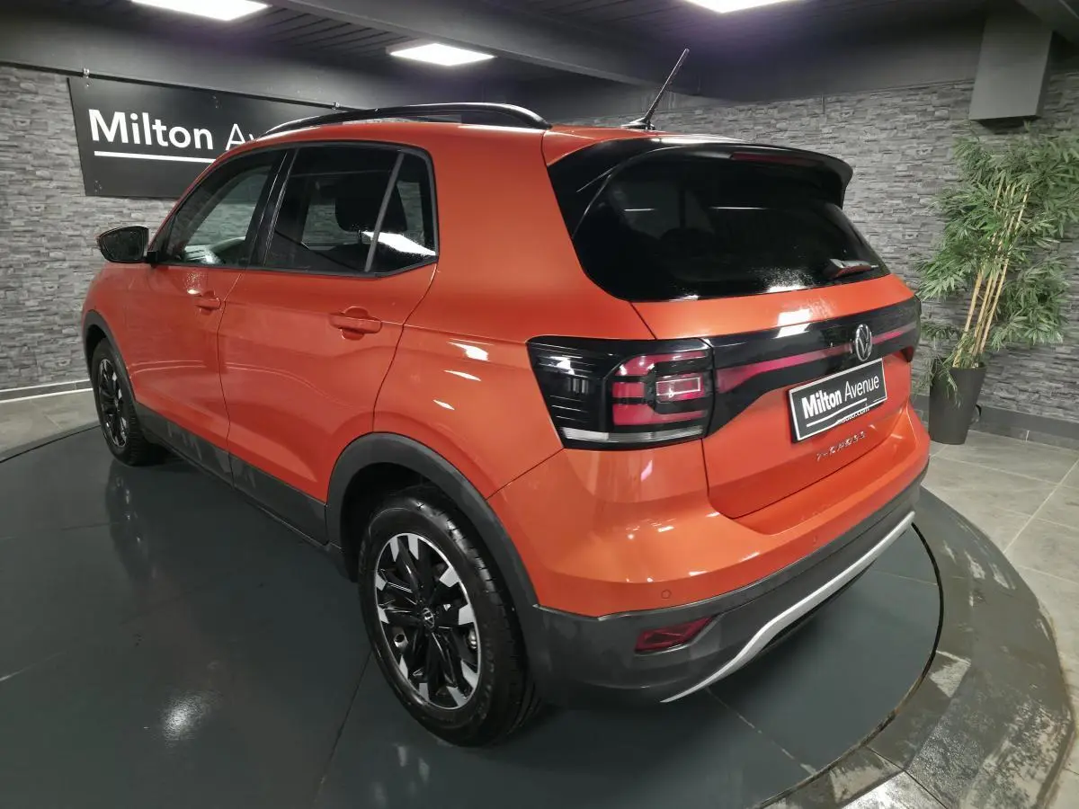 Vue 3/4 arrière gauche d'un Volkswagen T-Cross orange Energy avec vitres arrière surteintées et jantes alliage noires.
