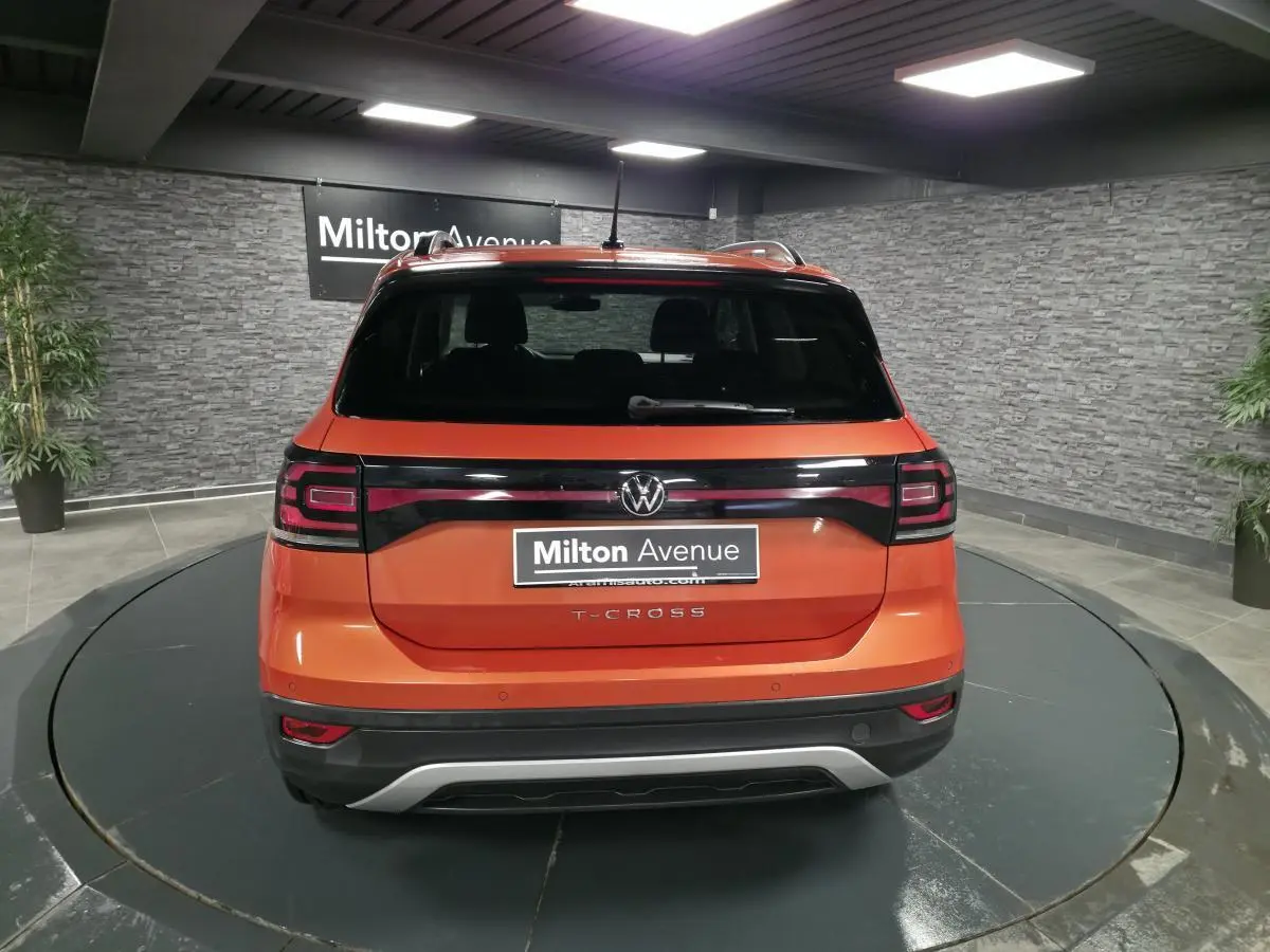 Vue arrière d'un Volkswagen T-Cross orange métallisé avec feux arrière noirs et logo VW central.