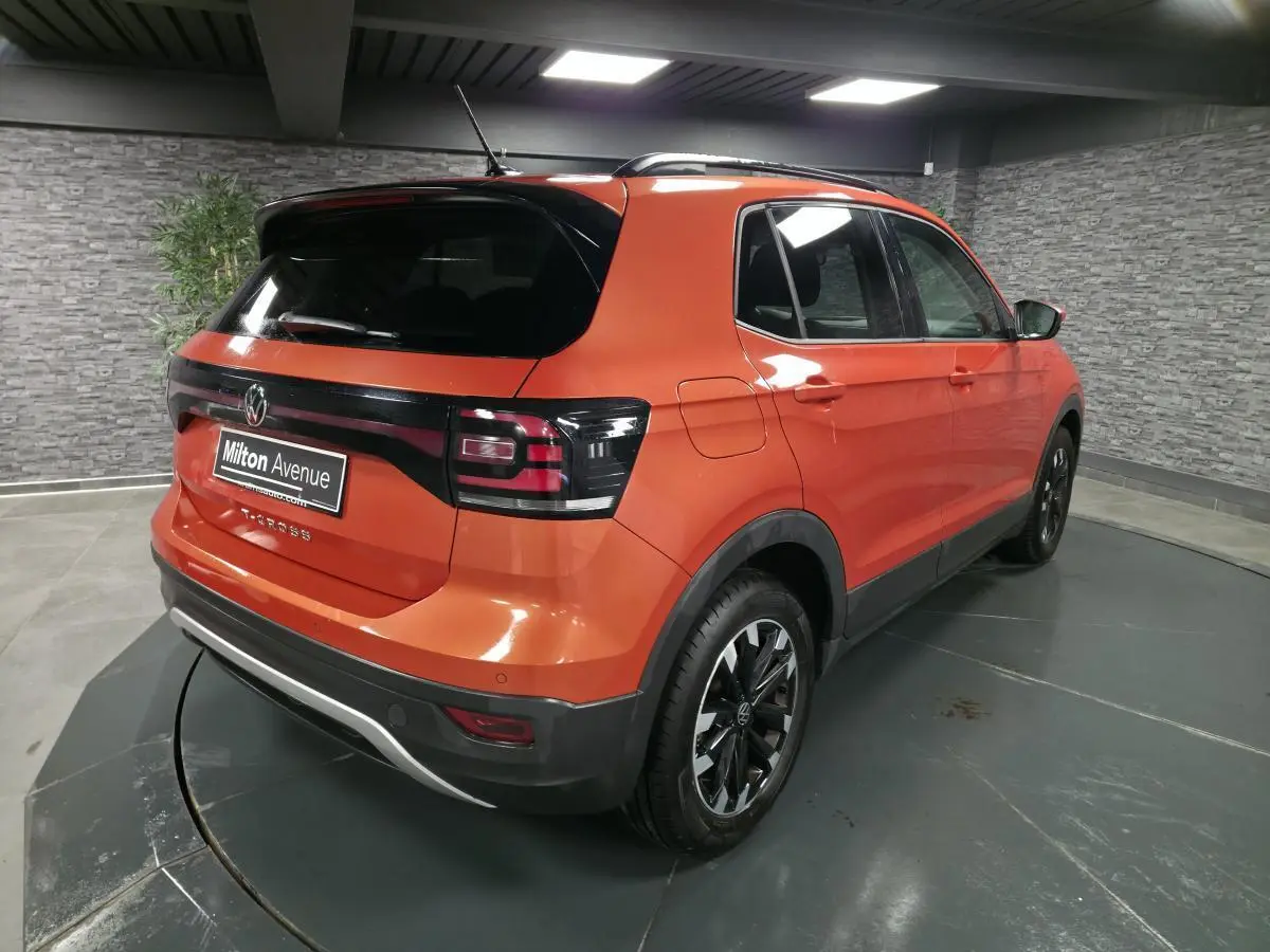 Vue 3/4 arrière droite d'un Volkswagen T-Cross orange métallisé avec vitres arrière surteintées et jantes alliage noires.