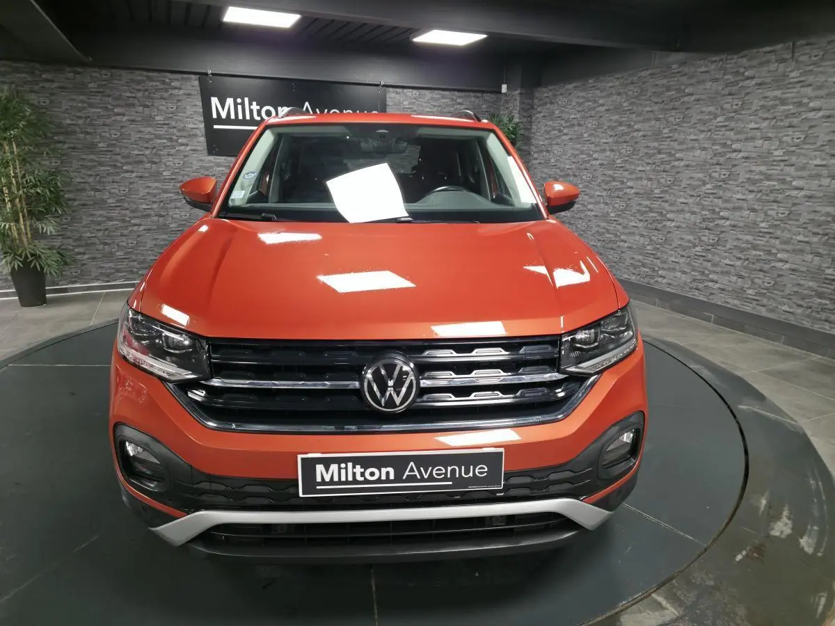 Vue avant d'un Volkswagen T-Cross orange métallisé avec calandre noire et détails chromés, en showroom.