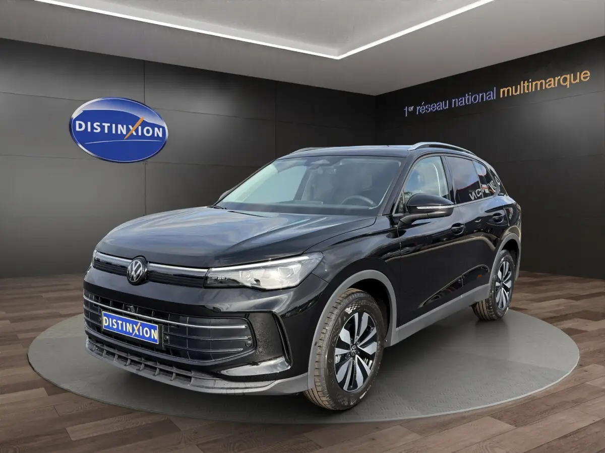 Volkswagen Tiguan noir en 3/4 avant droit, avec jantes bicolores et calandre épurée dans un showroom.