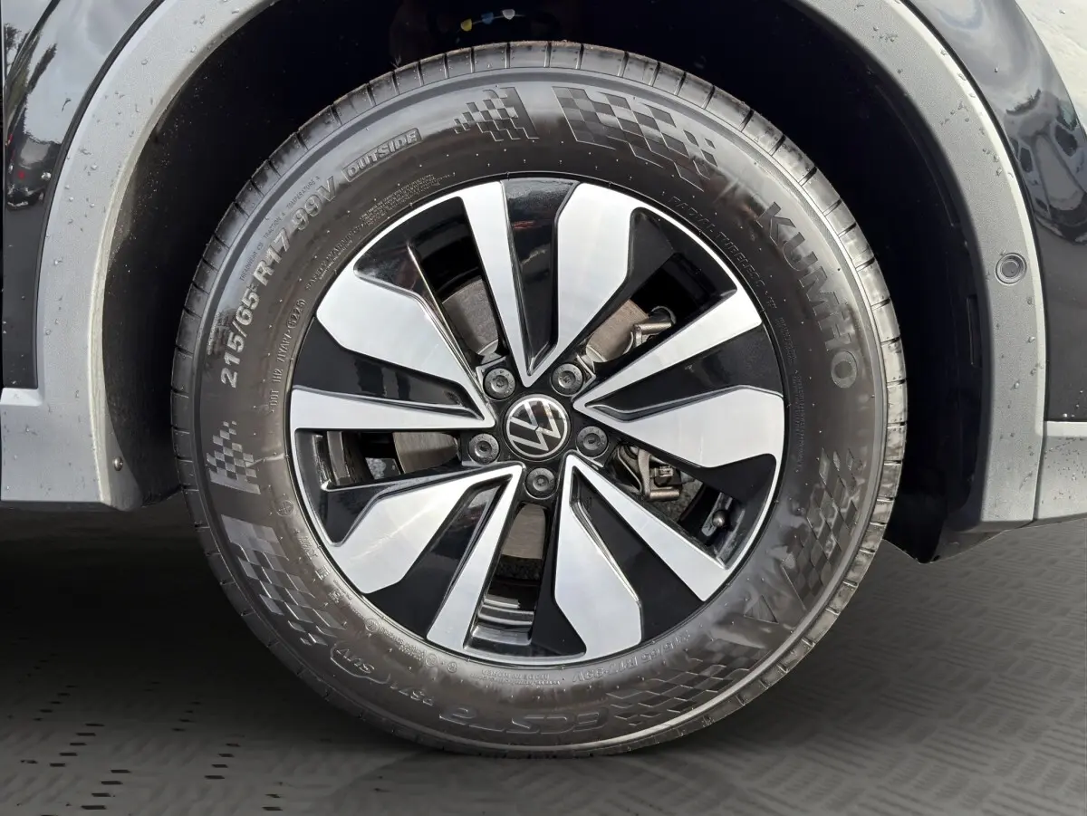 Gros plan sur la roue avant droite noire du Volkswagen Tiguan avec jante alliage bicolore et logo VW central.