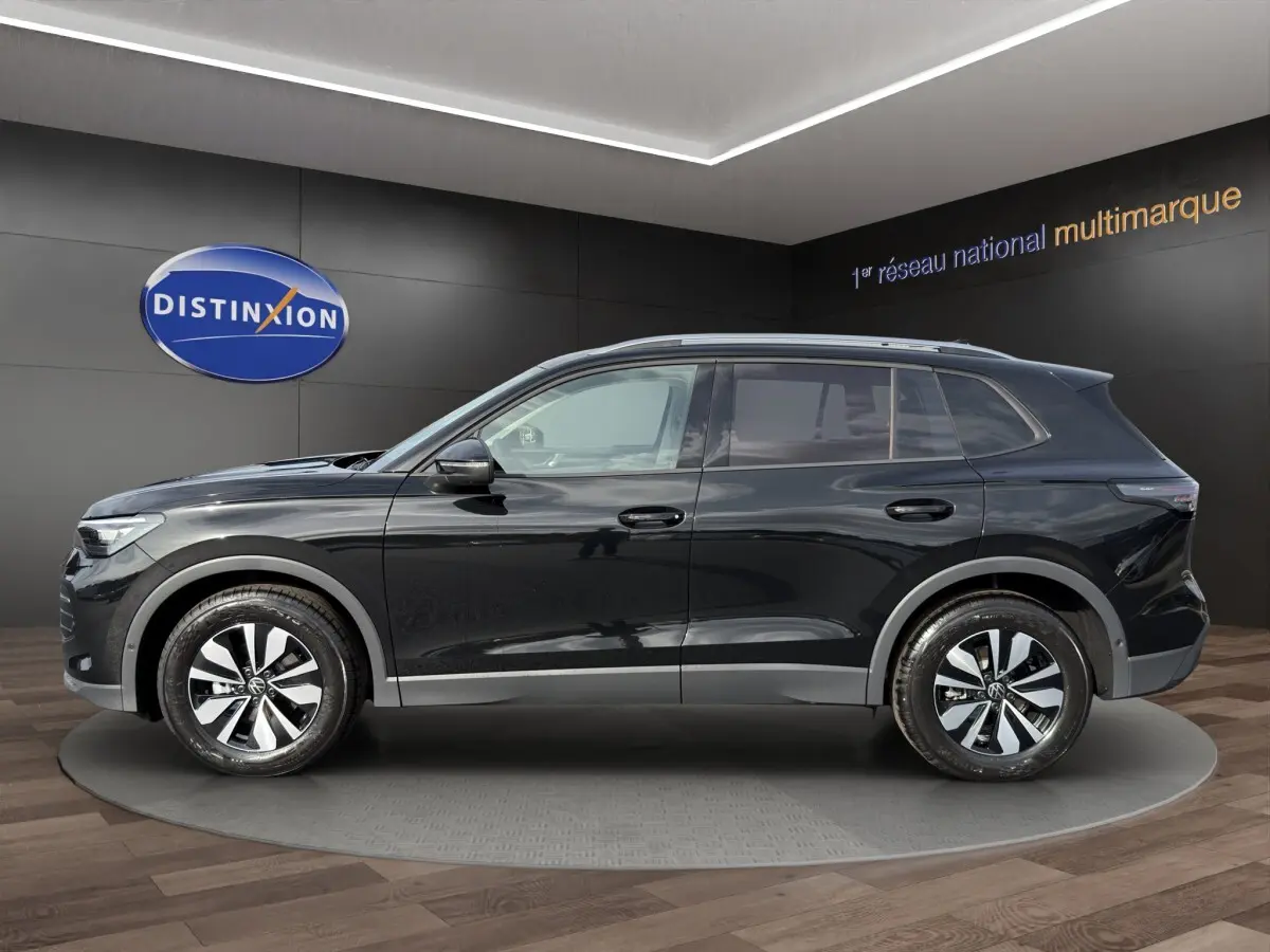 Profil côté gauche du Volkswagen Tiguan noir 2026 avec jantes alliage et rails de toit noirs en showroom.