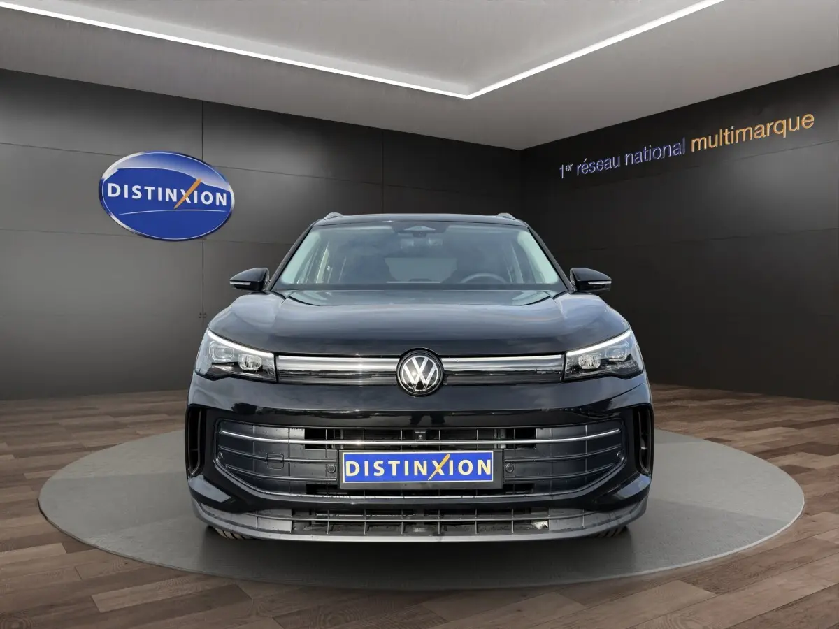 Vue frontale d'un Volkswagen Tiguan noir avec calandre large et logo VW centré, en showroom Distinxion.