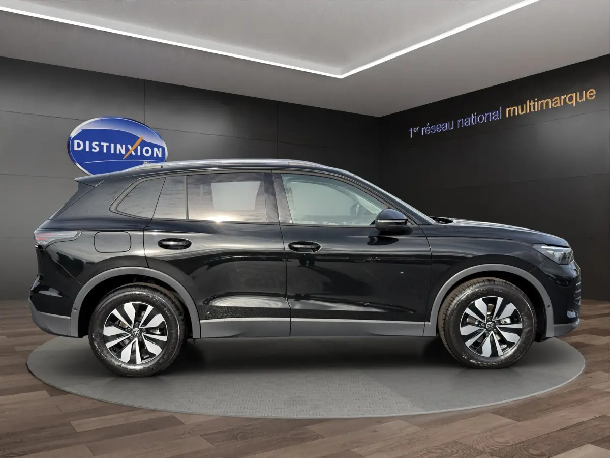 Volkswagen Tiguan noir vue de profil côté gauche, avec jantes modernes et lignes épurées en intérieur showroom.