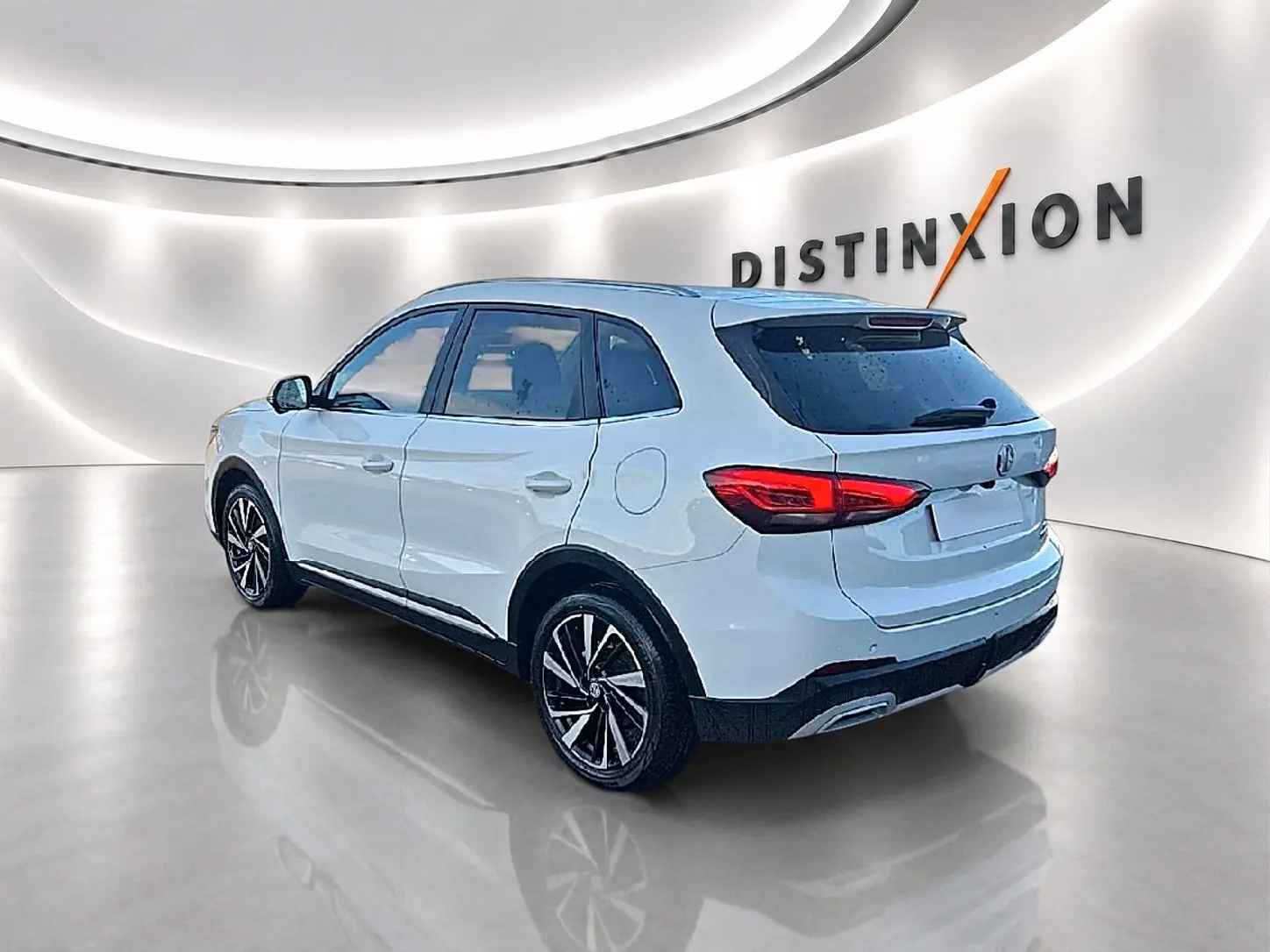 Vue 3/4 arrière droite d'un MG Motor ZS blanc 2026 avec jantes alliage et feux arrière LED dans un showroom lumineux.