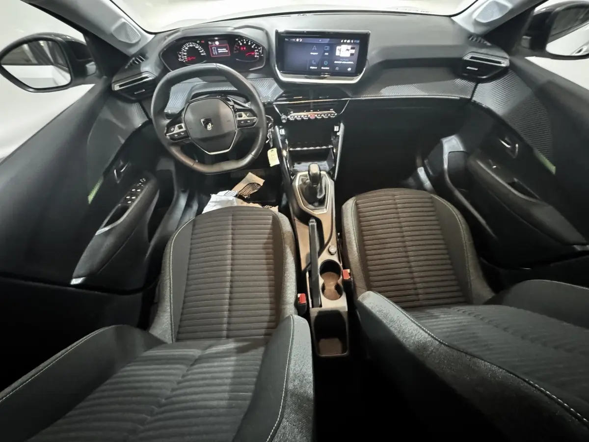 Vue intérieure avant de la Peugeot 208 PureTech 75 S&S Active 2024, sièges noirs et tableau de bord avec écran tactile central.