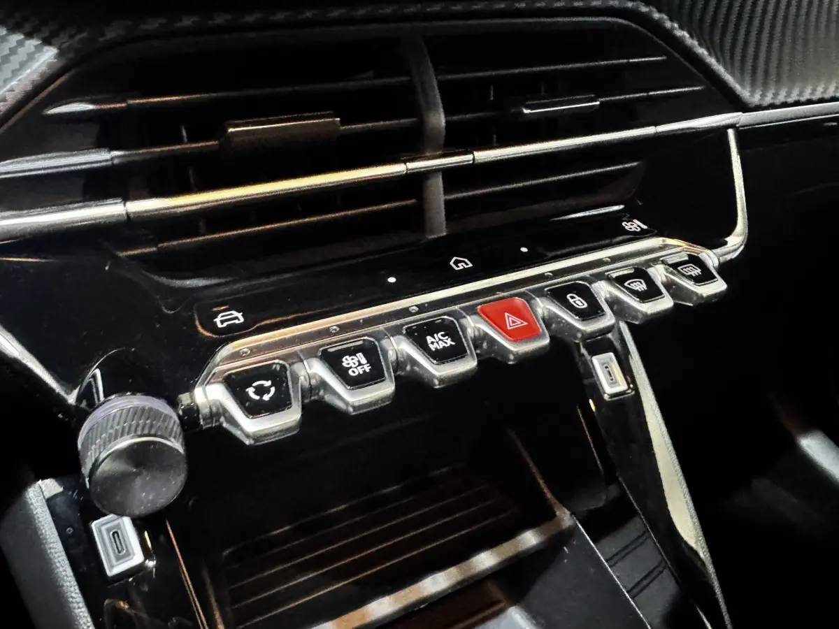 Gros plan sur la console centrale noire du Peugeot 208 2024 avec boutons de commande et port USB visible.
