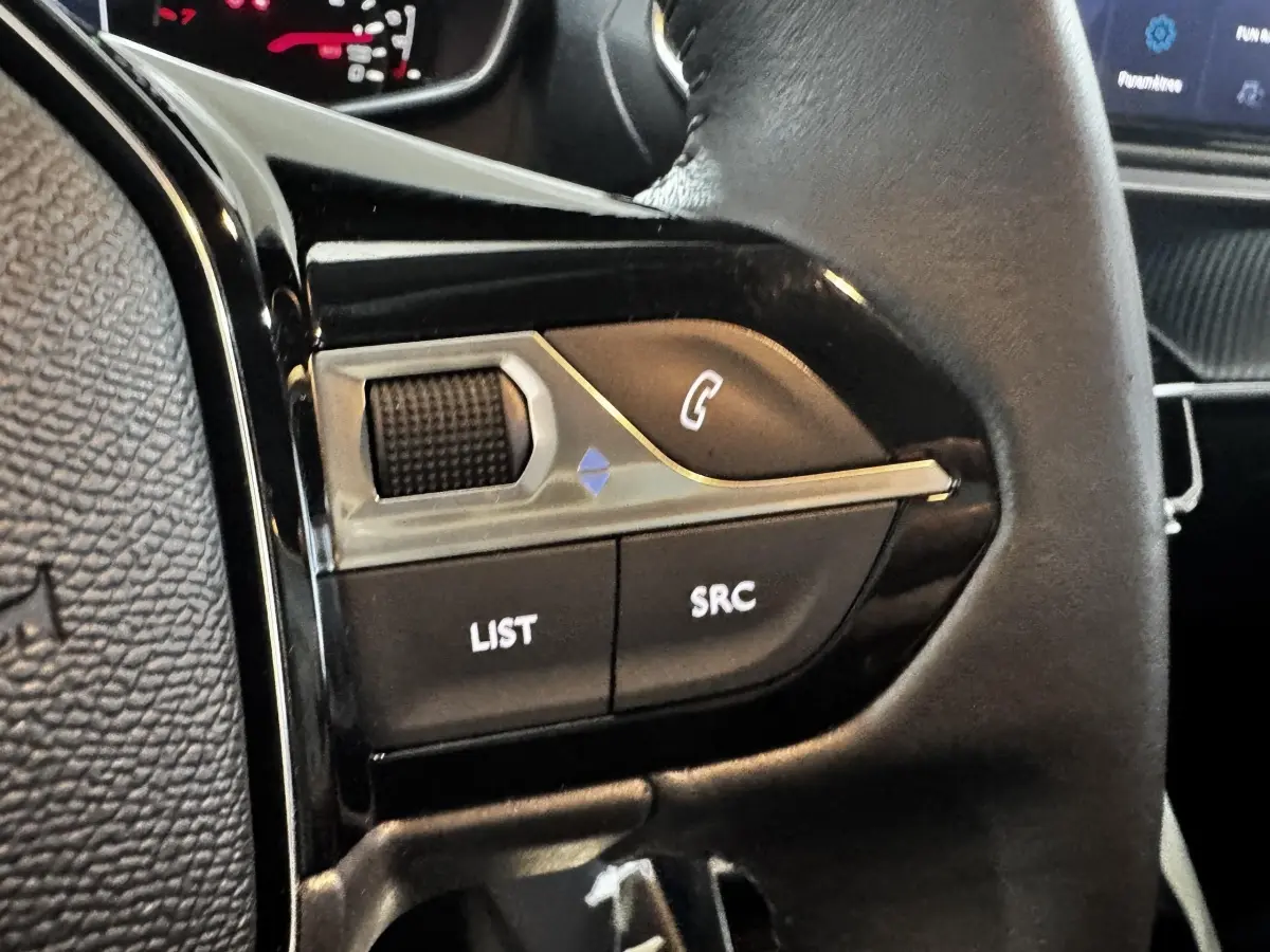 Gros plan sur les commandes gauche du volant cuir de la Peugeot 208 PureTech 75 S&S Active 2024, intérieur noir.
