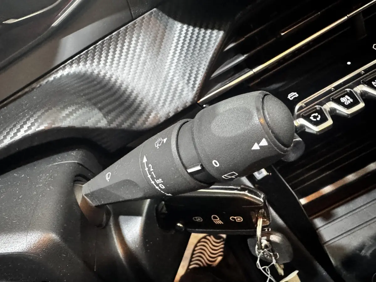 Gros plan sur la commande d’essuie-glace noire et la clé insérée dans le contacteur d’une Peugeot 208 blanche, intérieur noir.