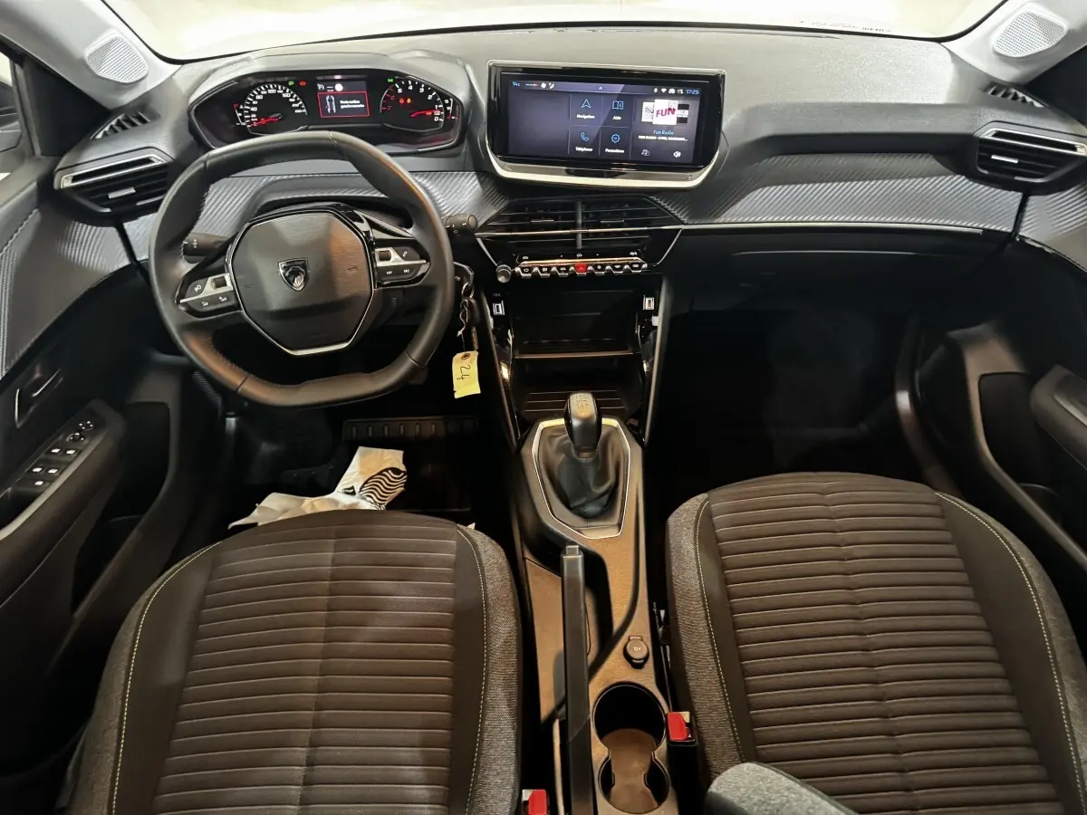 Vue intérieure avant du Peugeot 208 PureTech 75 S&S Active 2024, tableau de bord noir avec écran tactile central et volant cuir multifonctions.