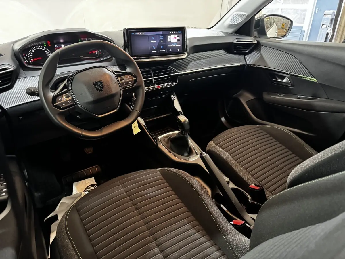 Vue intérieure avant droite du tableau de bord et des sièges noirs de la Peugeot 208 PureTech 75 S&S Active 2024.