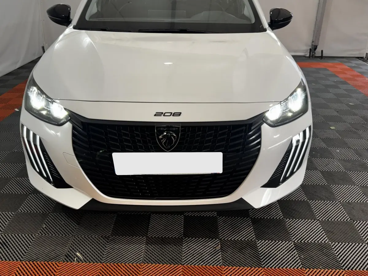 Vue avant d'une Peugeot 208 PureTech 75 S&S Active blanche avec phares LED allumés et calandre noire distinctive.