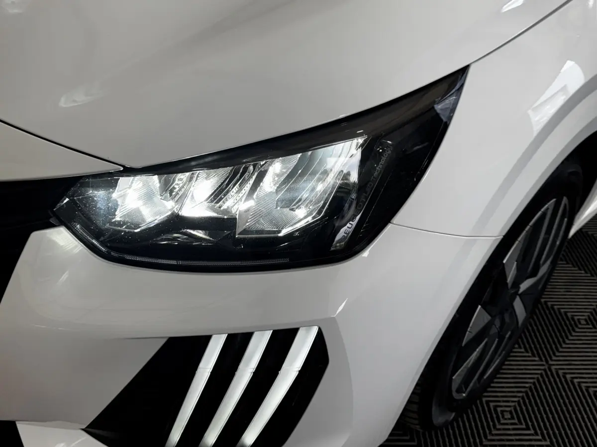 Gros plan sur le phare avant gauche et la calandre blanche d'une Peugeot 208 PureTech 75 S&S Active 2024.