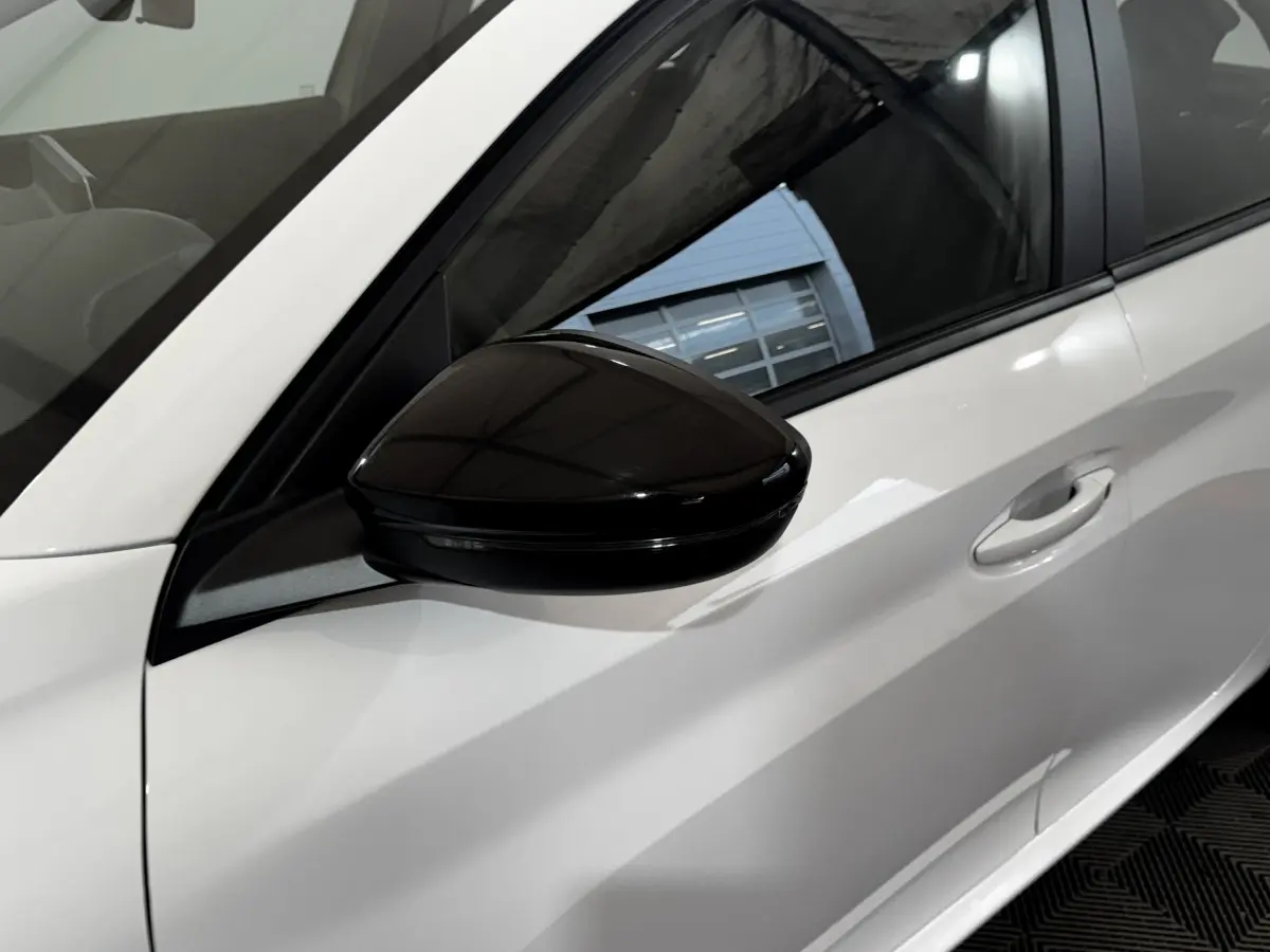 Gros plan sur le rétroviseur noir et la porte côté gauche d'une Peugeot 208 blanche vue de profil.