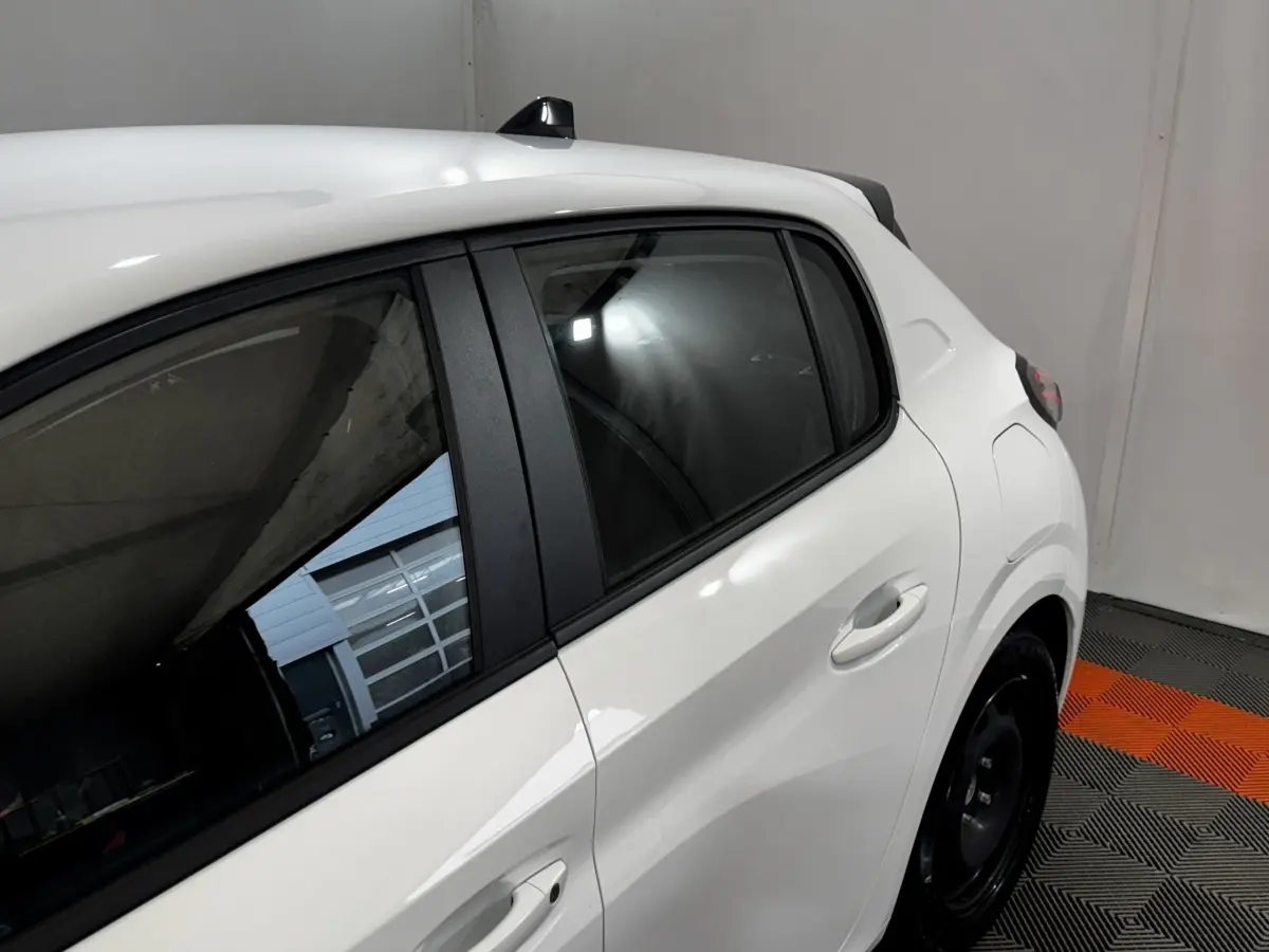 Vue latérale droite rapprochée d’une Peugeot 208 blanche, mettant en valeur la porte arrière et la vitre teintée.