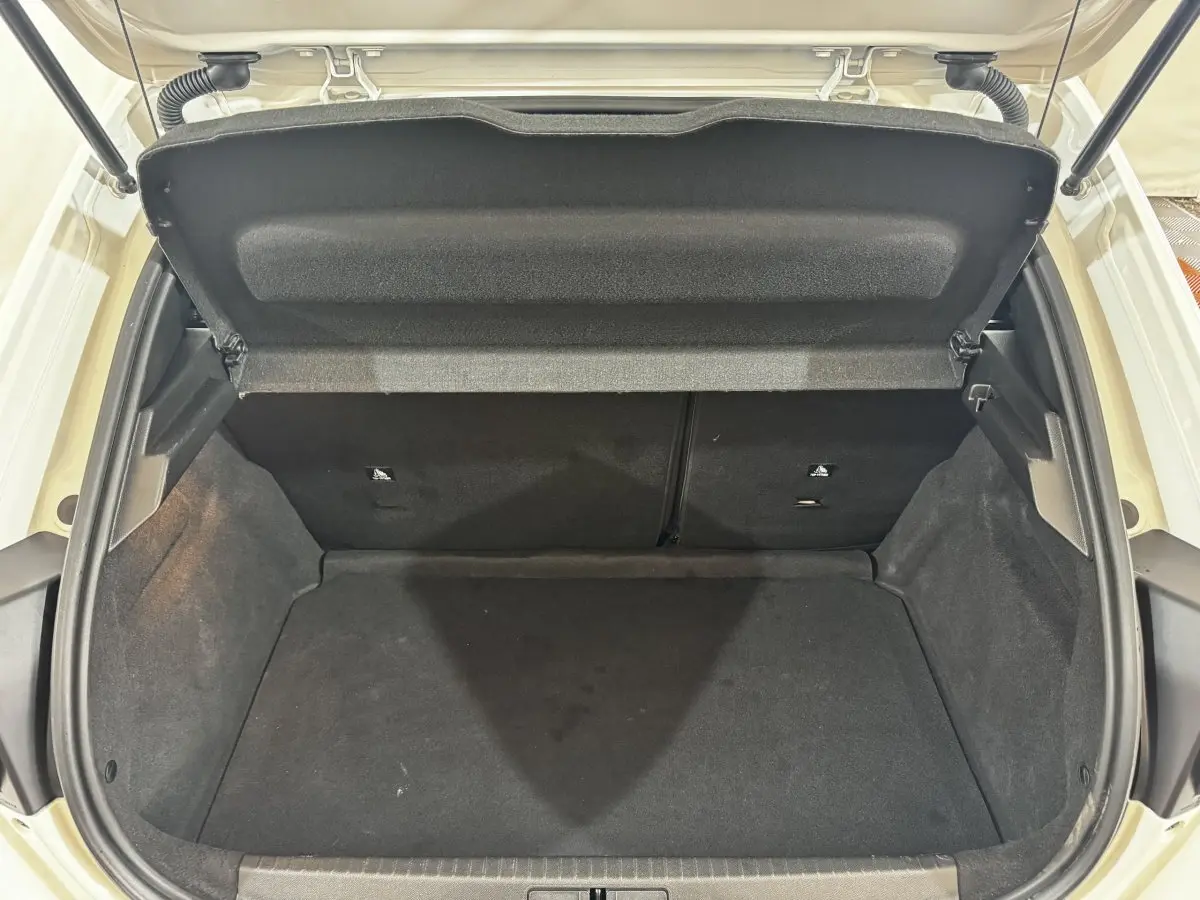 Coffre ouvert vu de face d'une Peugeot 208 blanche, montrant l'espace de chargement vide et la tablette arrière.