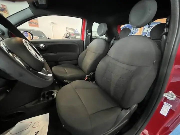 Intérieur de la FIAT 500 rouge 2023, vue côté gauche montrant les sièges avant en tissu noir et le volant.