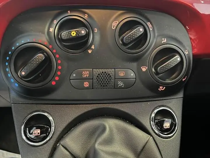 Gros plan sur la console centrale rouge de la Fiat 500 2023, montrant les commandes de climatisation et la boîte manuelle.
