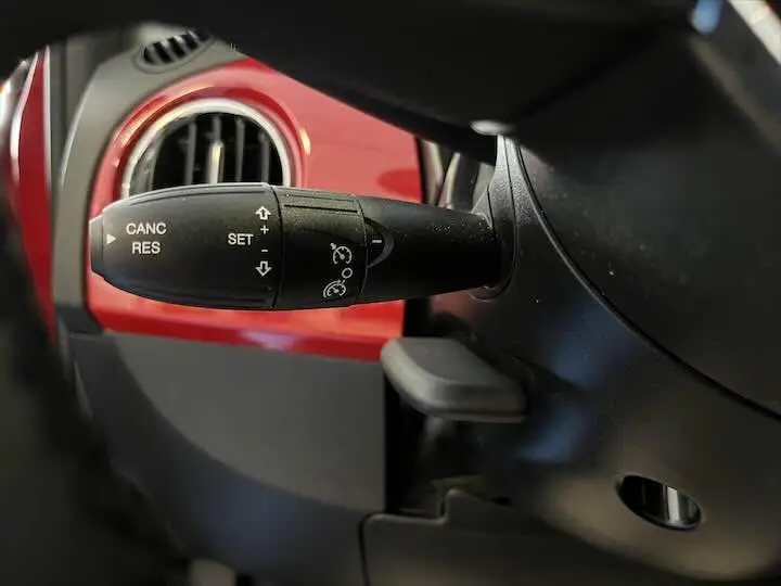Le levier de régulateur de vitesse dans l'habitacle d'une FIAT 500 rouge, vue rapprochée côté gauche.
