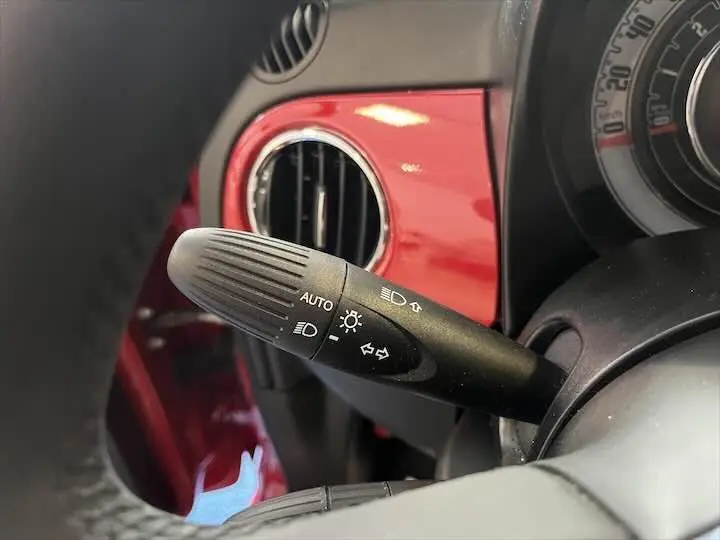Gros plan sur la commande des phares et clignotants dans l'habitacle rouge vif d'une Fiat 500 2023.