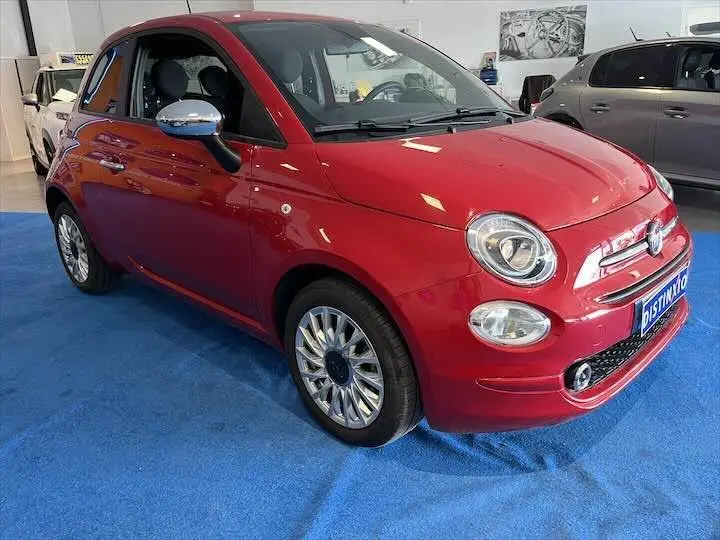 Vue 3/4 avant d'une FIAT 500 rouge brillante avec jantes alliage et rétroviseurs chromés en intérieur showroom.