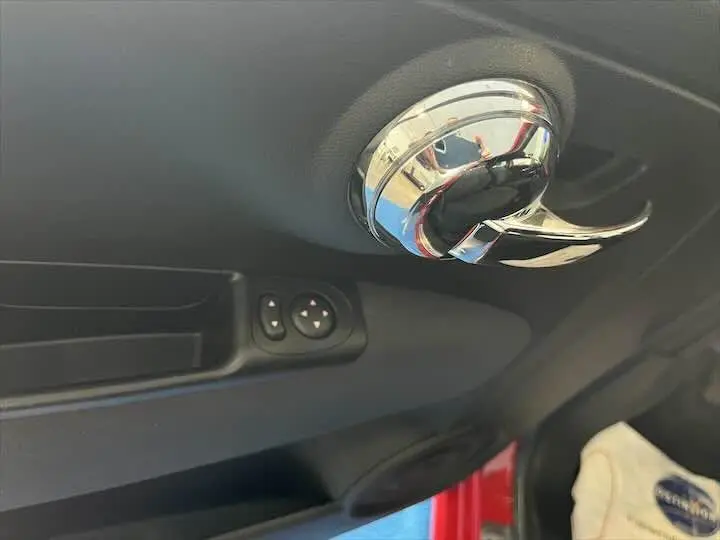 Poignée de porte intérieure chromée côté gauche avec commandes de réglage des rétroviseurs sur FIAT 500 rouge 2023.