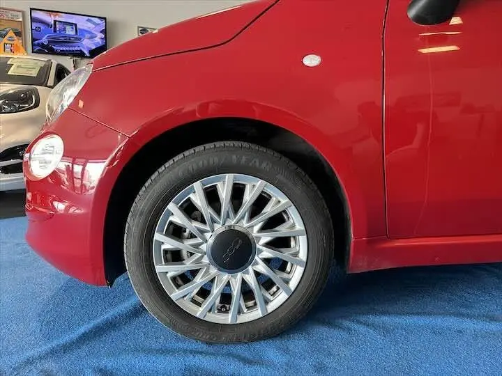 Gros plan sur la roue avant gauche d'une FIAT 500 rouge 2023 avec jante argentée en étoile, vue en intérieur showroom.