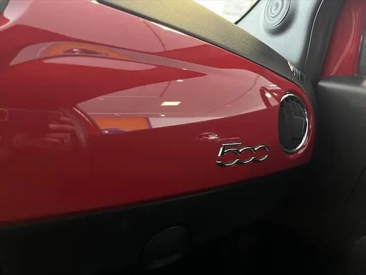 Détail intérieur du tableau de bord rouge brillant de la Fiat 500 avec logo 500 et sortie d'air ronde côté droit.