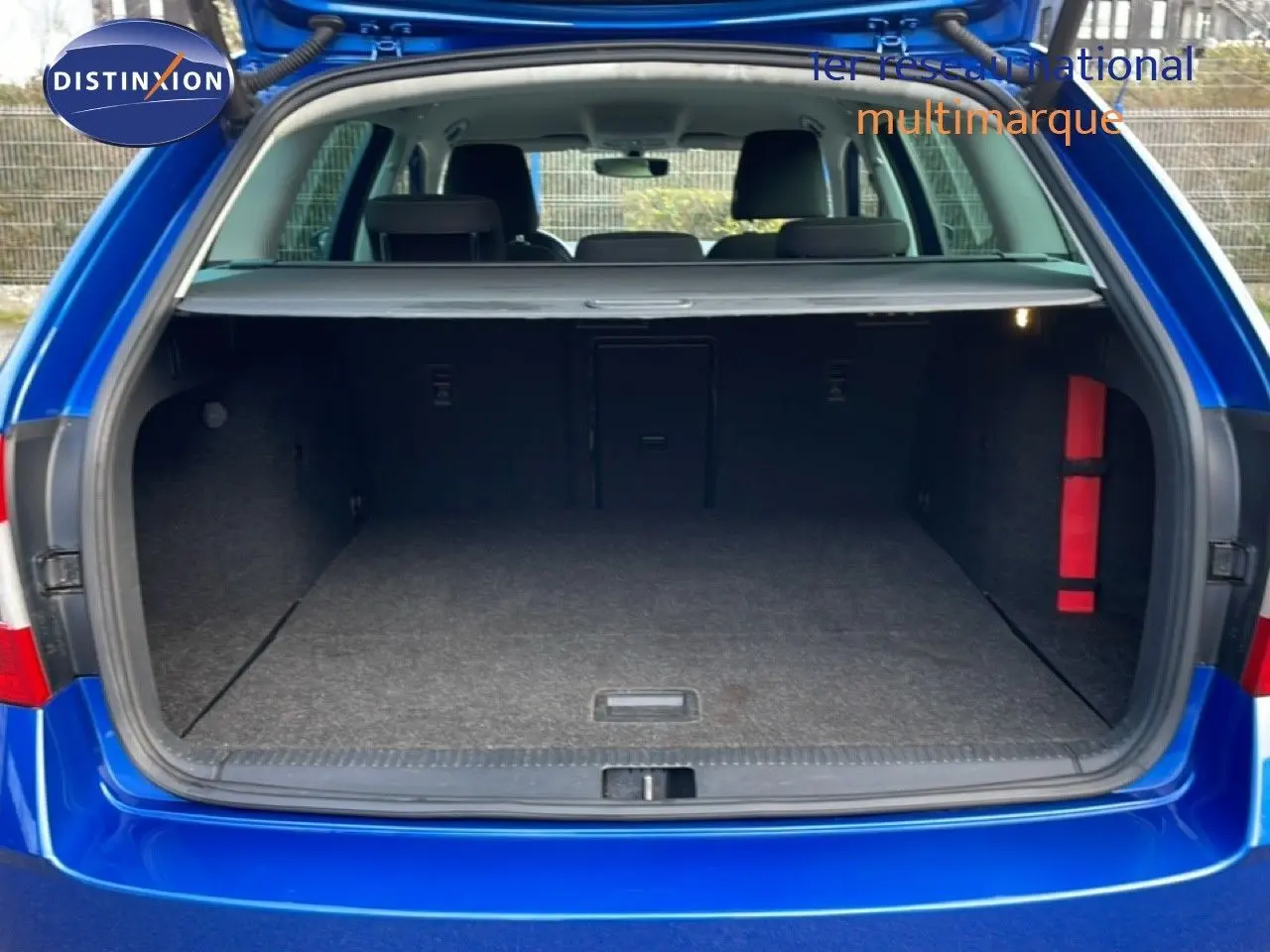 Coffre ouvert vu de l'arrière d'une Skoda Octavia Combi bleu racing metal, intérieur spacieux et tapis gris.