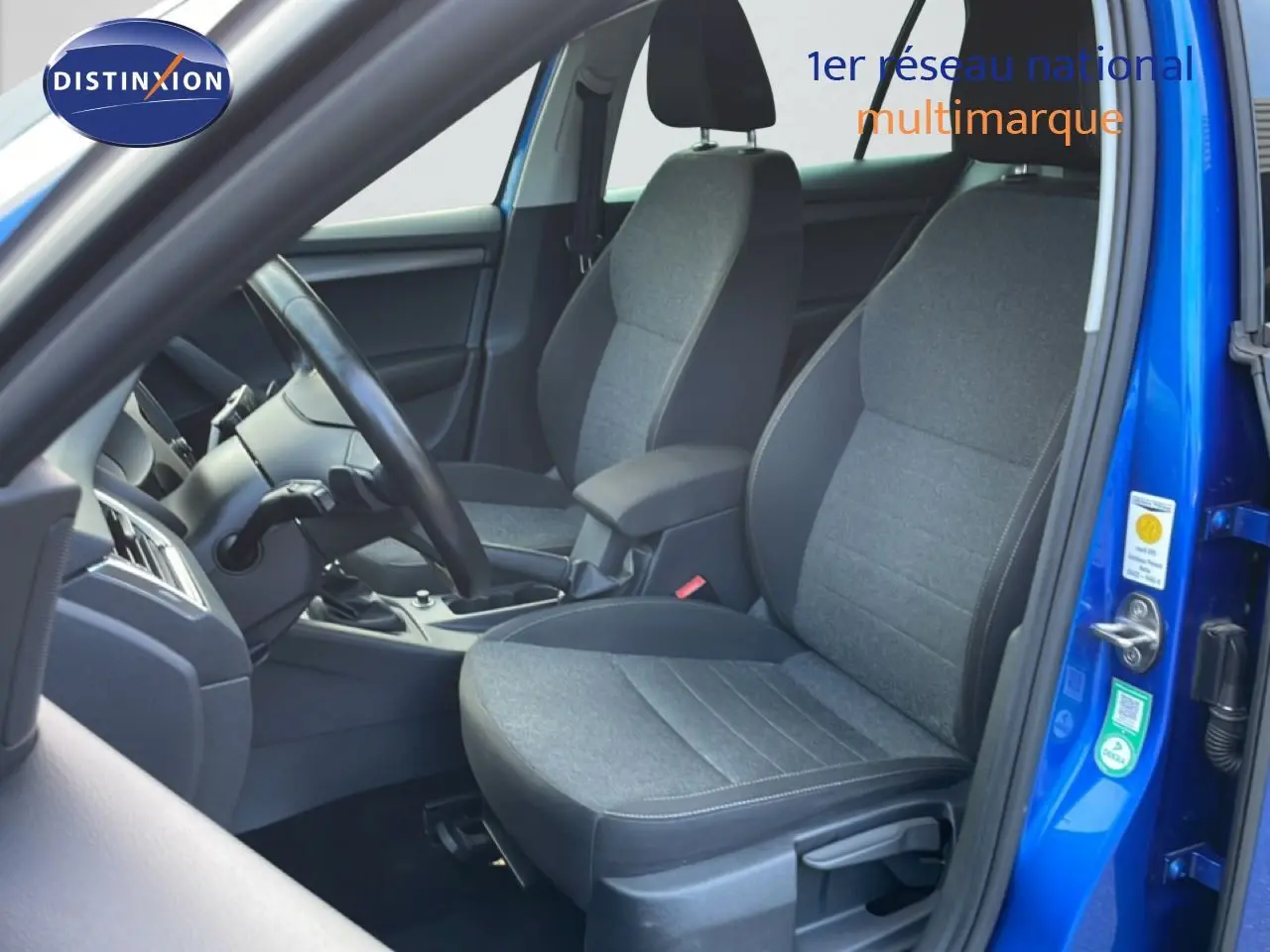 Vue intérieure côté conducteur de la Skoda Octavia Combi bleu racing, sièges tissu gris et volant noir visible.