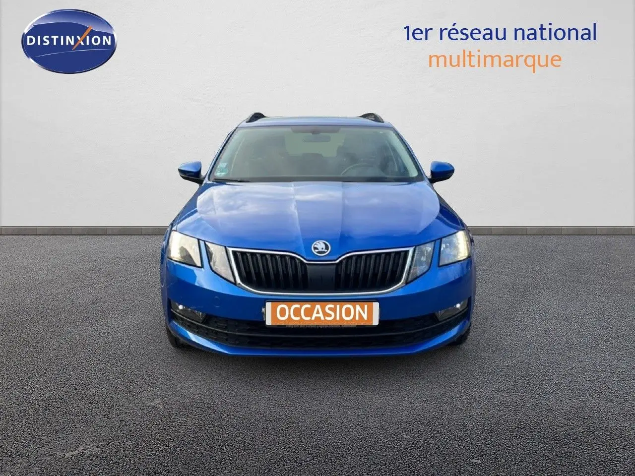Vue frontale d'une Skoda Octavia Combi bleu racing métal, avec calandre noire et phares allumés sur fond neutre.