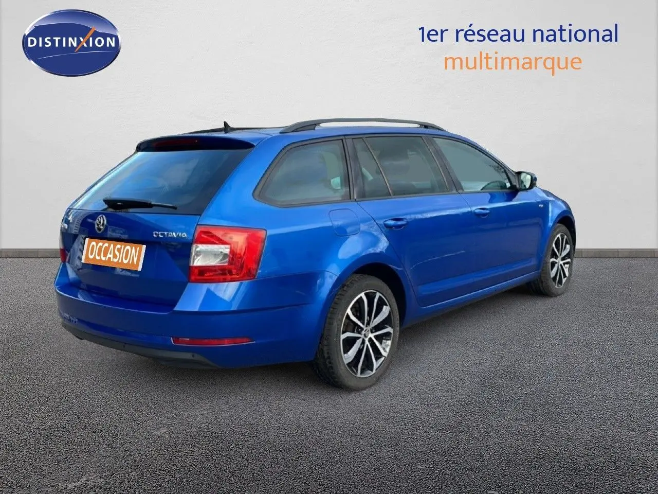 Vue 3/4 arrière droite d'une Skoda Octavia Combi 2019 bleu racing metal avec jantes alliage et barres de toit.