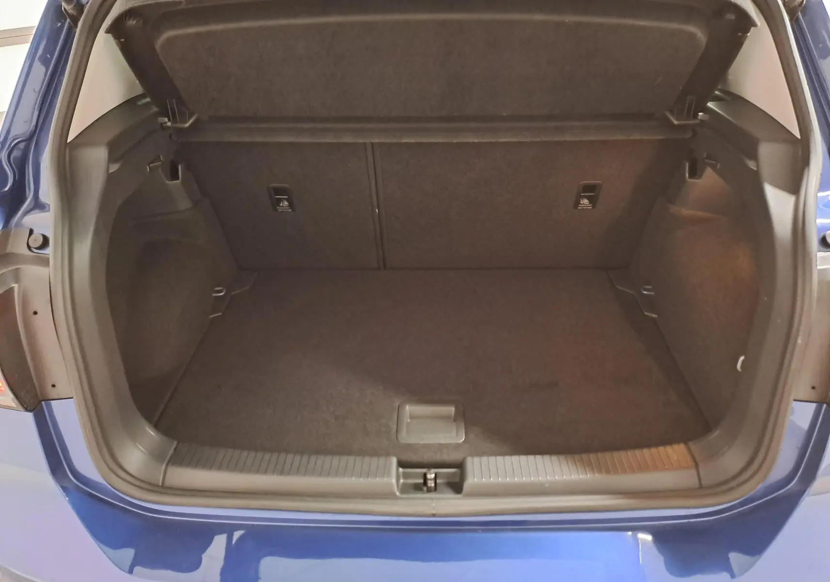 Coffre ouvert vu de l'arrière d'un Volkswagen T-Cross 2022 bleu récif, intérieur spacieux et tapis noir.
