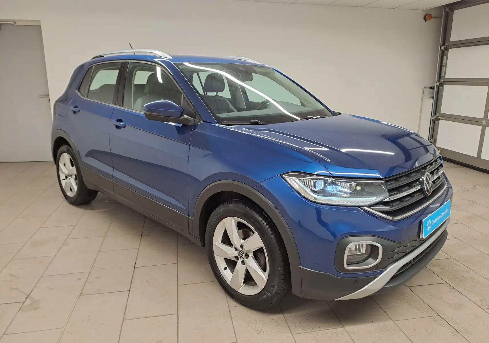 Volkswagen T-Cross Bleu Récif en vue 3/4 avant droit, avec phares allumés et jantes alliage cinq branches.