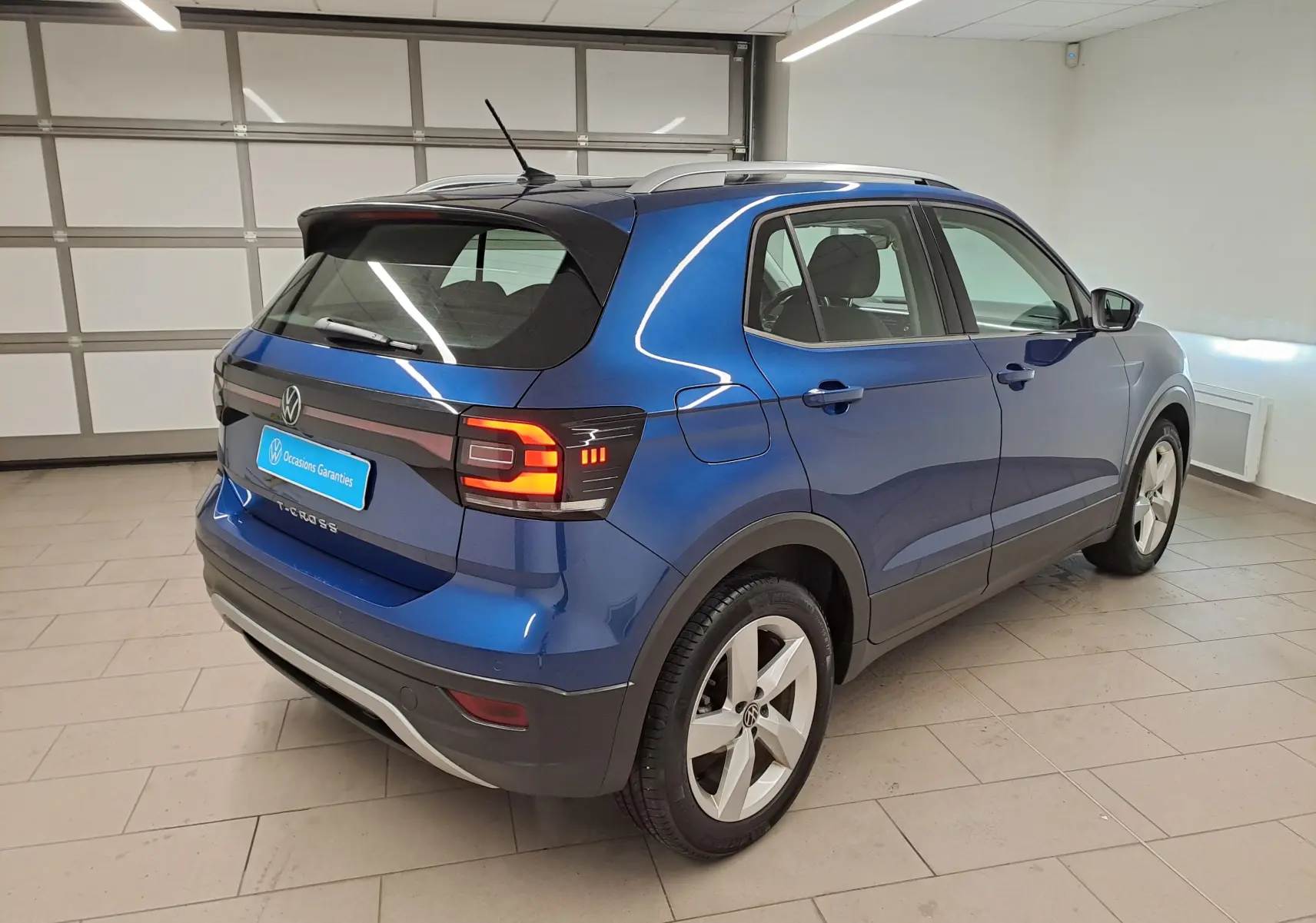 Volkswagen T-Cross Bleu Récif en 3/4 arrière droit, avec feux arrière allumés dans un garage.
