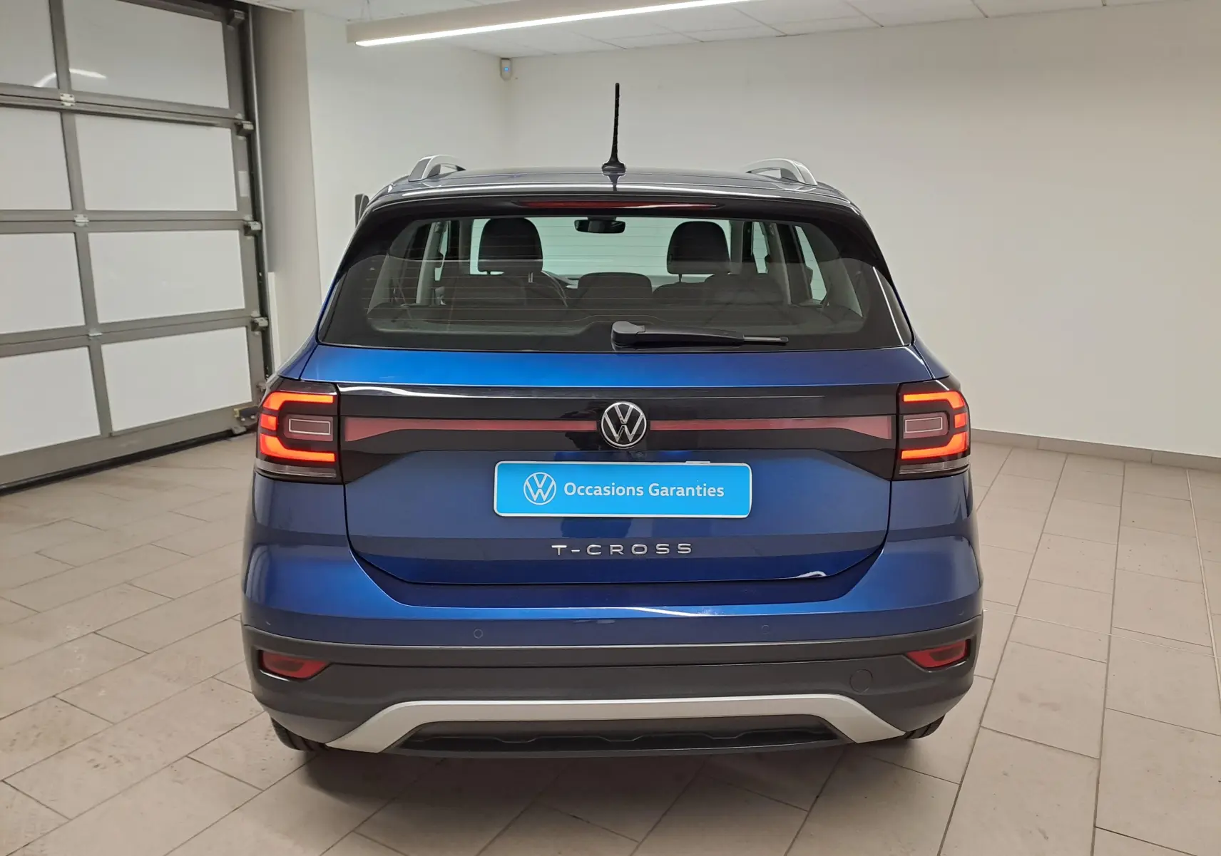 Vue arrière d'un Volkswagen T-Cross bleu récif 2022 avec feux LED allumés dans un garage.