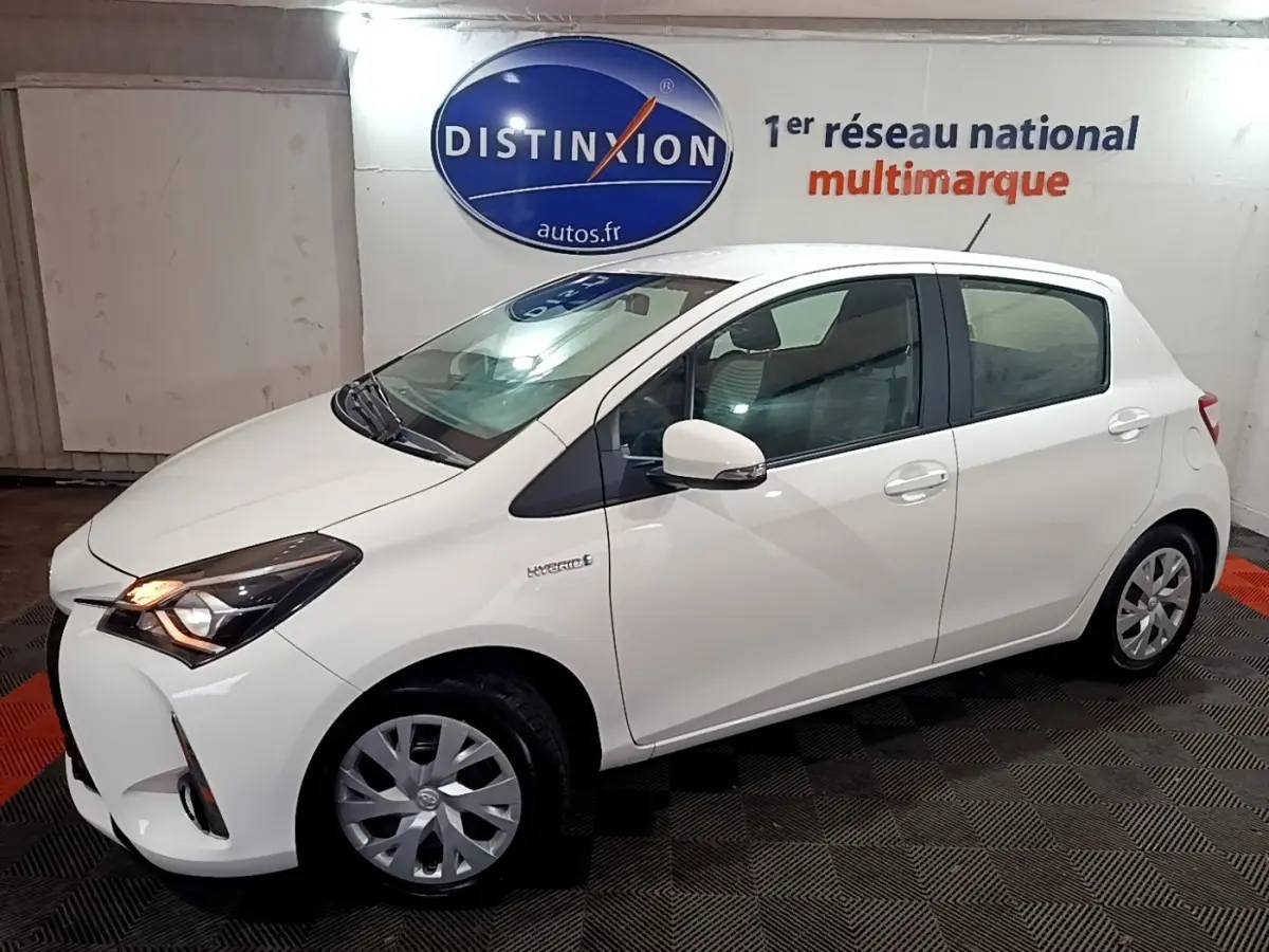 Toyota Yaris hybride blanche vue de profil côté gauche, avec phares allumés et jantes alliage simples.