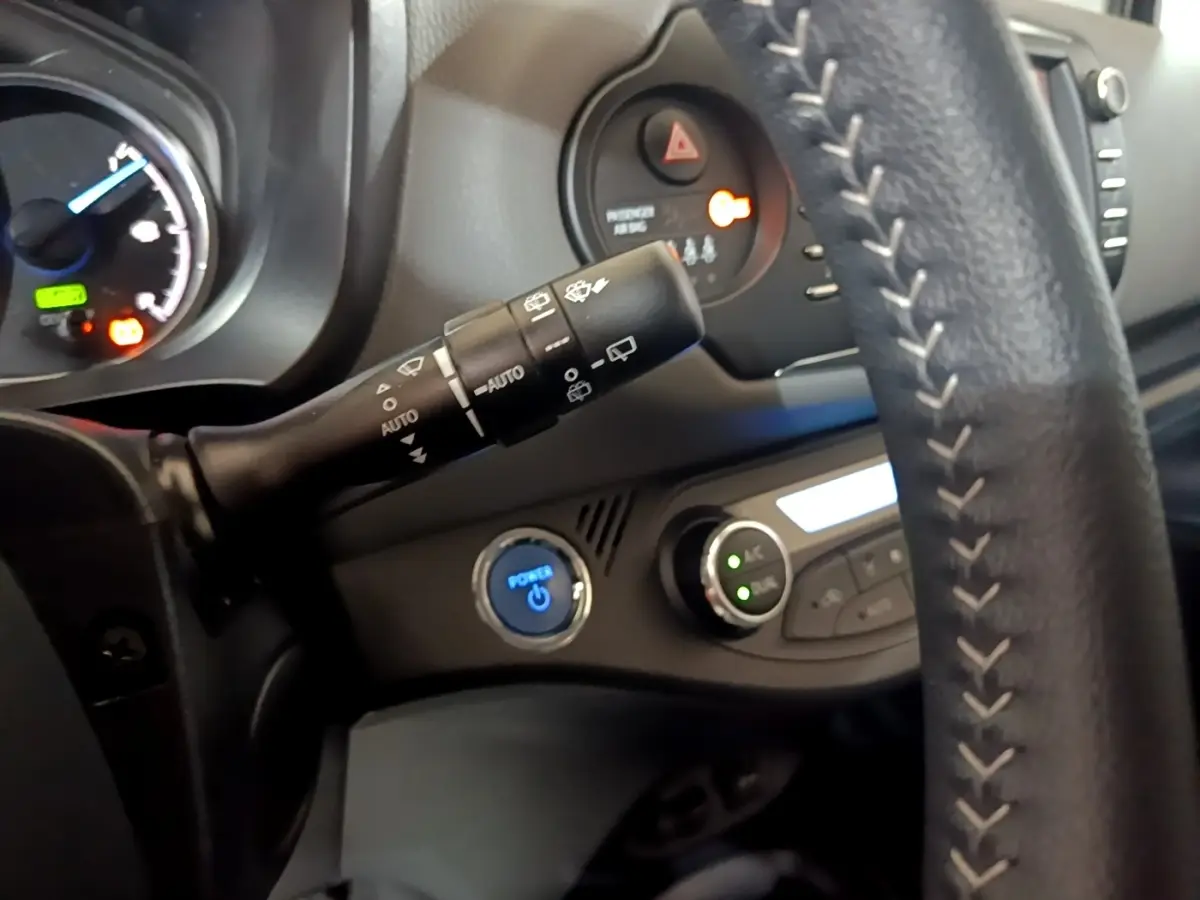 Gros plan sur le volant cuir et la commande d'essuie-glace de la Toyota Yaris hybride blanche, tableau de bord partiel visible.