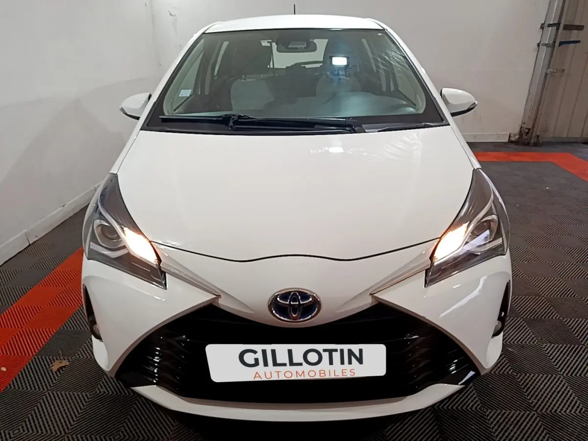 Vue avant d'une Toyota Yaris blanche 2019 avec phares allumés et calandre noire distinctive.