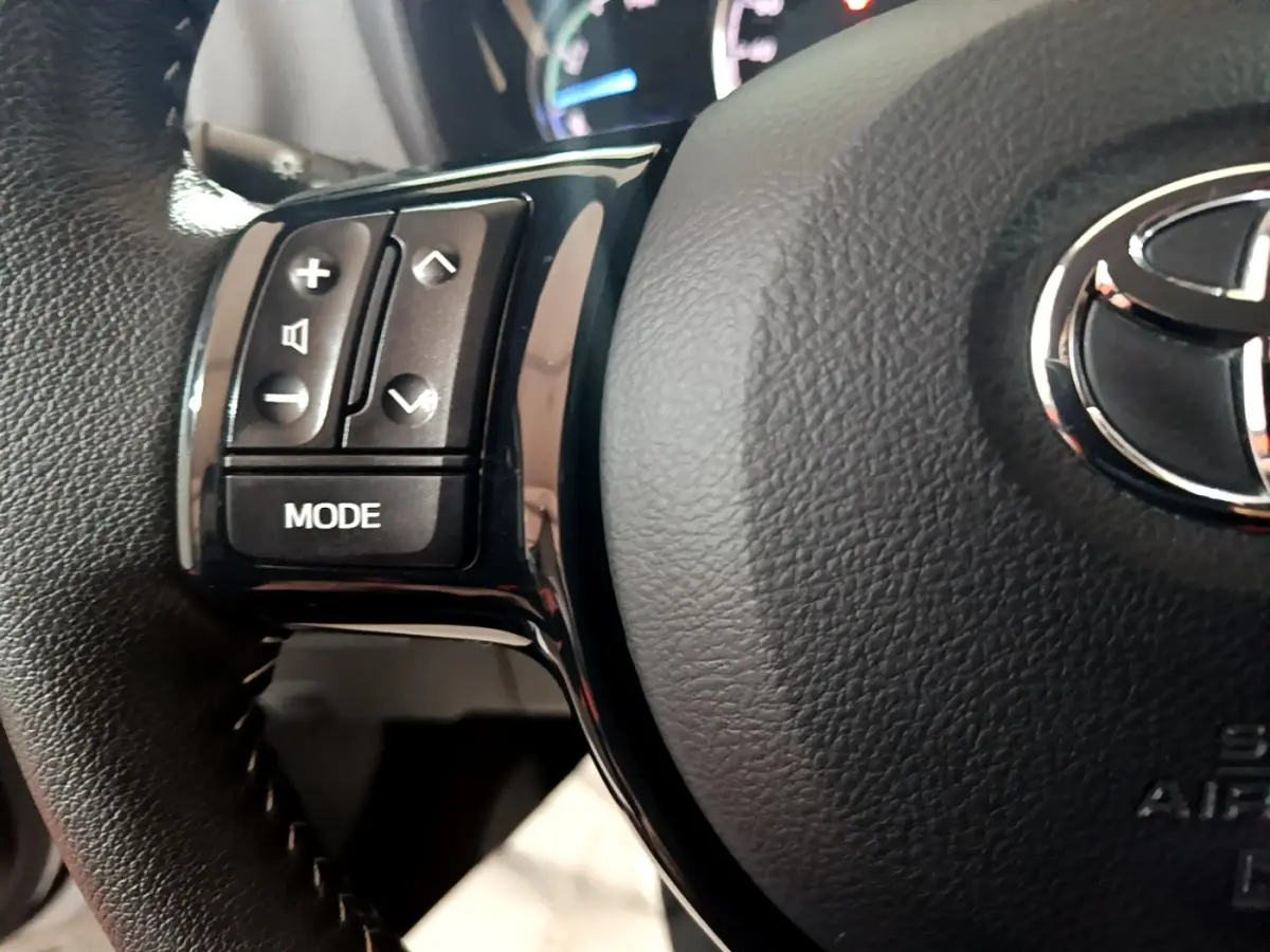 Gros plan sur le volant cuir noir de la Toyota Yaris 1.5 Hybrid, avec commandes audio et logo Toyota central argenté.